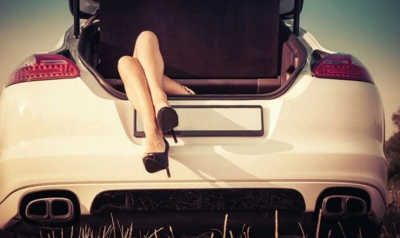Woman's legs and high heels hanging out of the trunk of a car