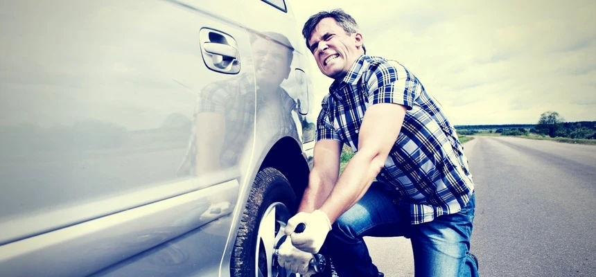Man struggling to change tire of car Man struggling to change tire of car