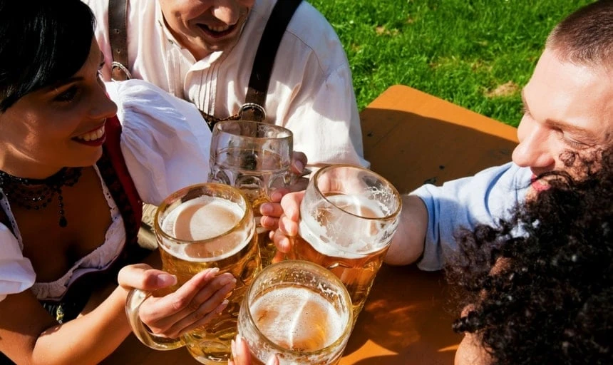 Group of four in traditional Bavarian dress, Lederhosen and Dirndl, drinking beer and smiling