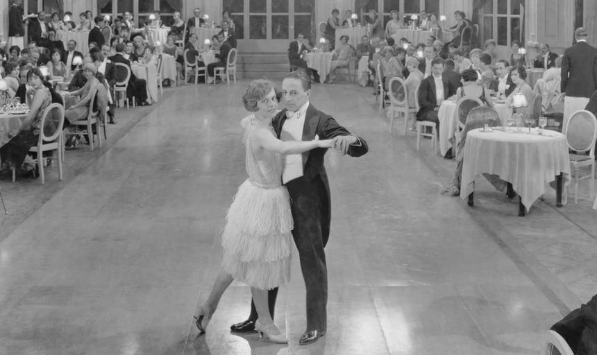 Man and woman ballroom dancing in the middle of the room with people watching at tables, black and white vintage