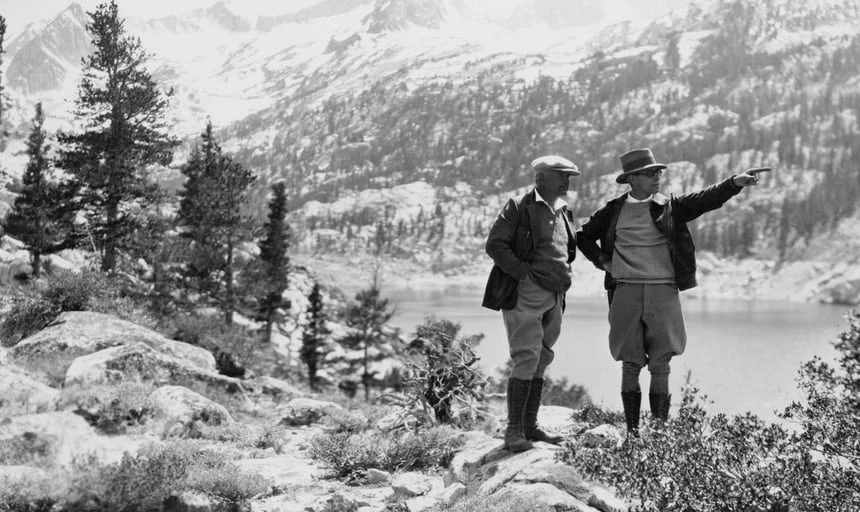 Two elderly men out hiking in the wilderness, one man pointing in the distance, in black and white