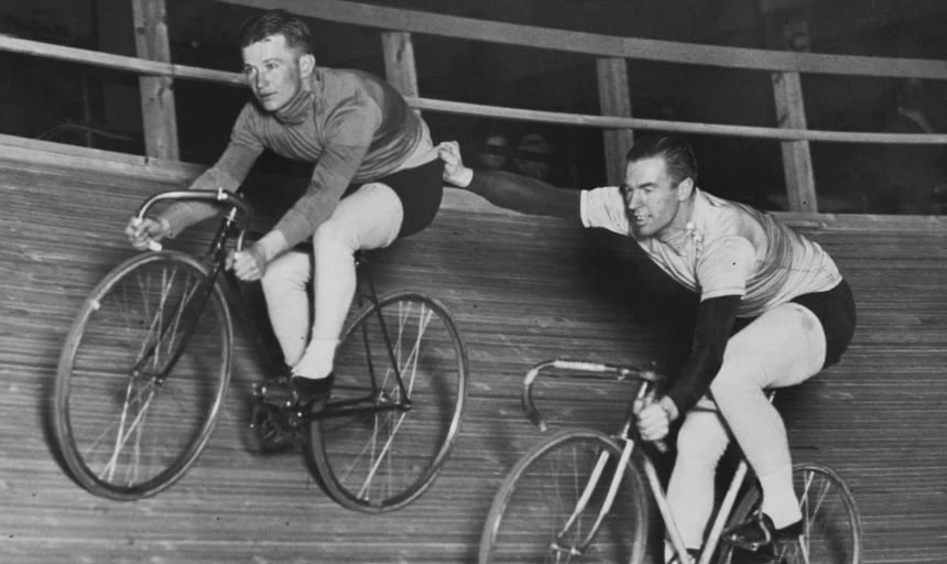 Vintage image of two men cycling, the man behind holding onto the one in front