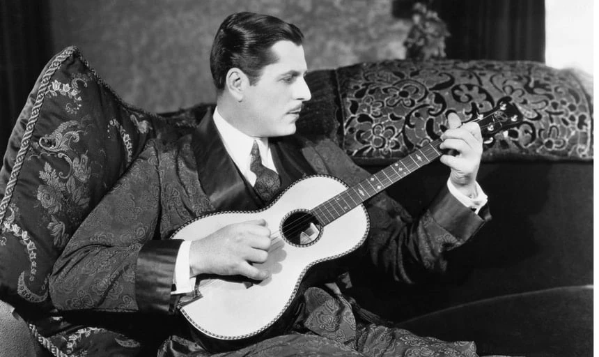 Vintage man playing an acoustic guitar in black and white in a robe