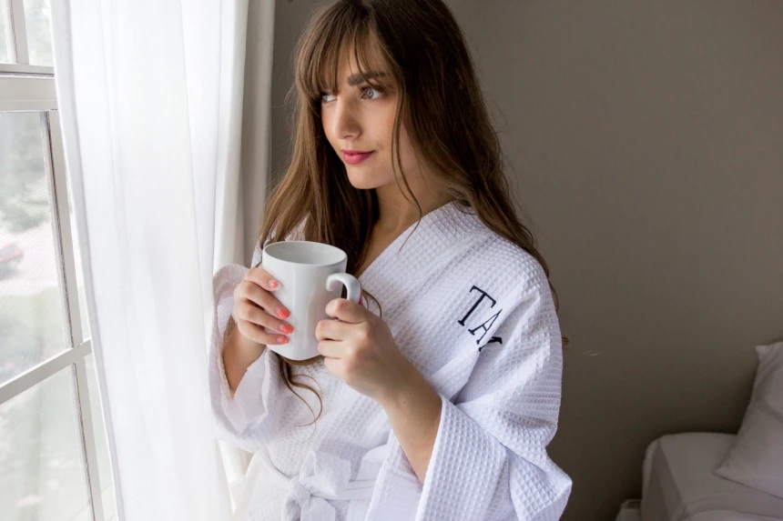 Luxor Linens Review (+ How to Keep Your Sheets Tight With the Bed Scrunchie) 70 Female model wearing Luxor Linens Lakeview Signature Egyptian Cotton Spa Robe while holding a coffee and looking out the window