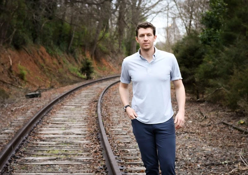model wearing western rise limitless merino wool polo standing near train tracks
