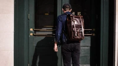 model wearing moral code leather rolltop backpack entering a door