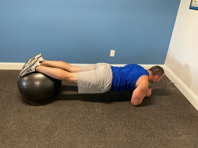 Fitness model performing plank exercise indoors with exercise ball
