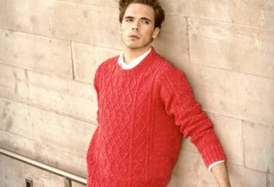 2020/10/Shetland-Sweaters_-Model-Leaning-Against-the-Wall-Wearing-a-Red-Sweater.jpgw3.webp
