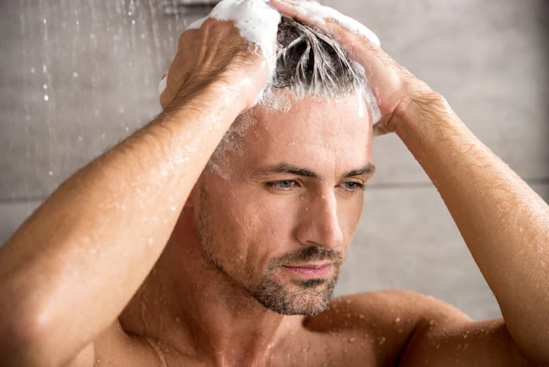 Man in shower shampooing hair serious face