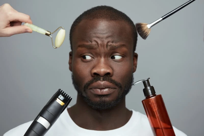 Black Man With Multiple Beauty Products Near His Face