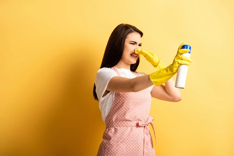 displeased housewife apron rubber gloves plugging hose hand while spraying